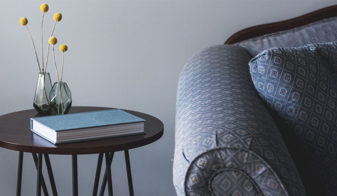 close up of patterned soft arm and cushion with side table and vases of flowers